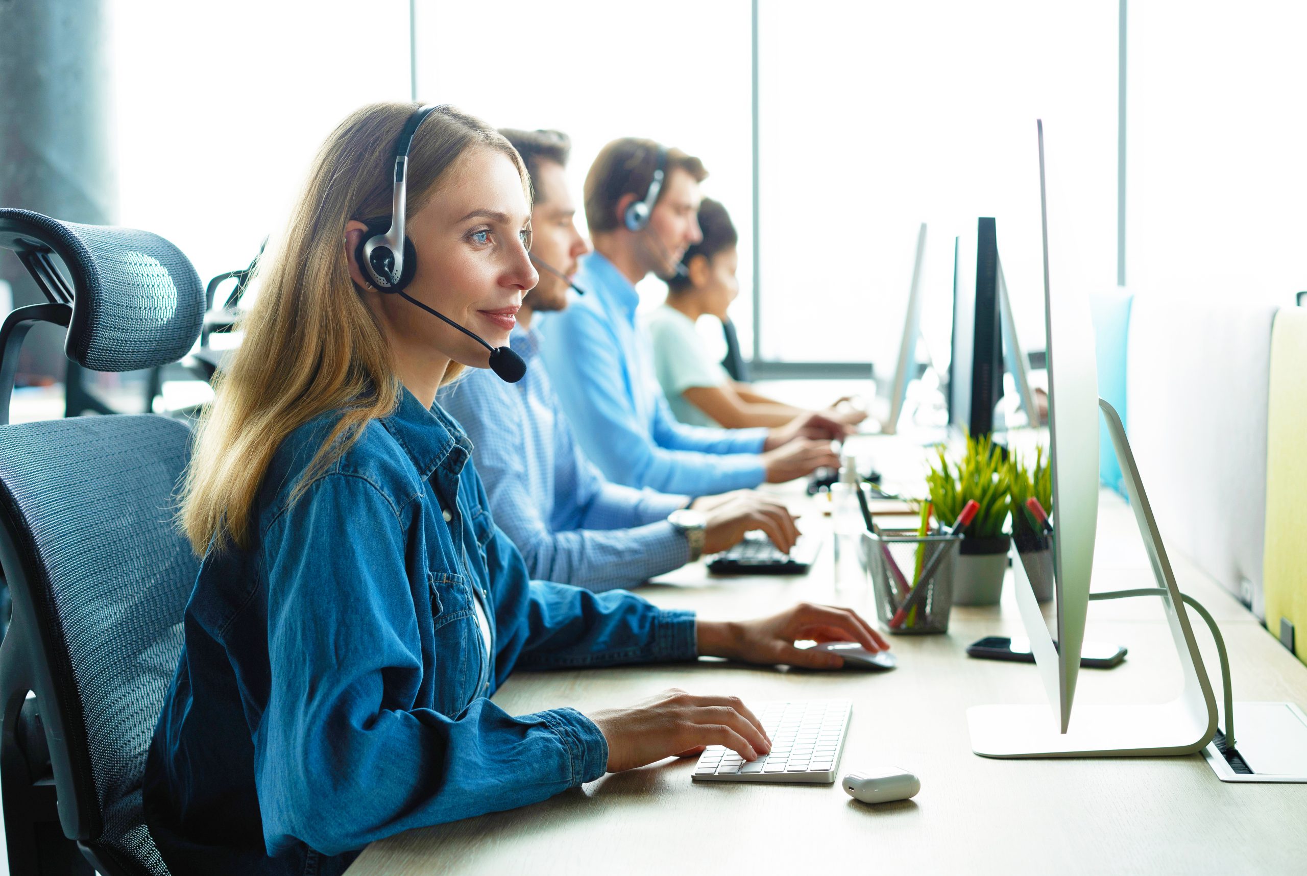 women with a microphone looking to a computer with 3 other peoples in the background while telesales