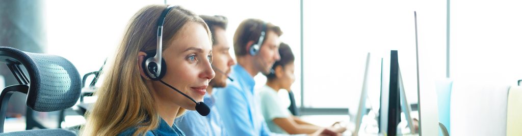 women with a microphone looking to a computer with 3 other peoples in the background in customer support