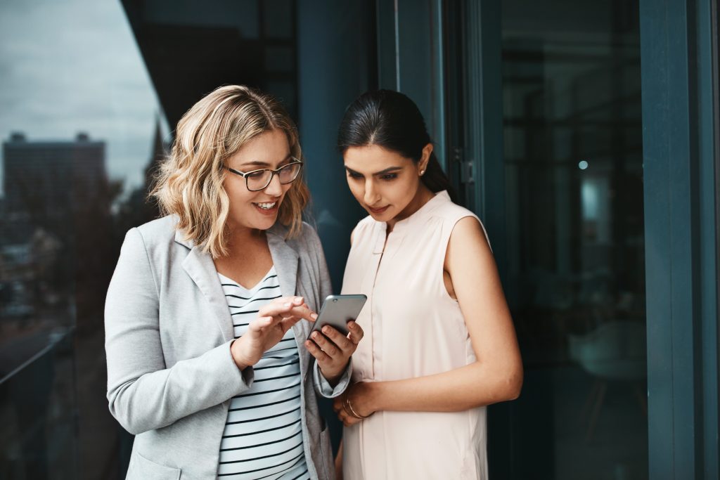 Two businesswomen using a cellphone checking out the trends in customer experience